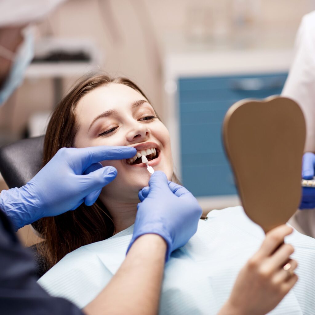 Young woman holding mirror as dentist shows sample veneer